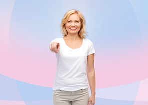 gesture, advertisement and people concept - smiling woman in blank white t-shirt pointing finger to you over pink and violet background