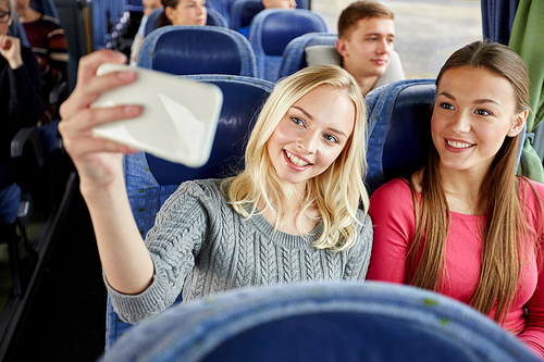 transport, tourism, road trip and people concept - happy young women or friends in travel bus taking selfie by smartphone