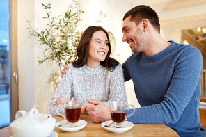 people, communication and dating concept - happy couple drinking tea and hugging at cafe or restaurant