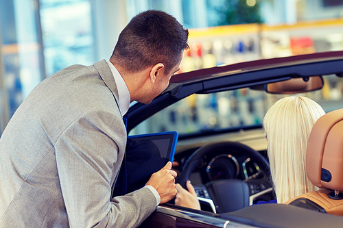 auto business, car sale, technology and people concept - woman and car dealer with tablet pc computer in auto show or salon