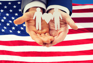 people, homosexuality, same-sex marriage and love concept - close up of happy male gay couple holding paper cutout love symbol over american flag background