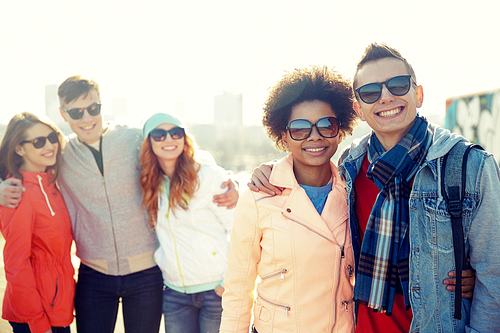 tourism, travel, people, leisure and teenage concept - group of happy friends in sunglasses hugging on city street