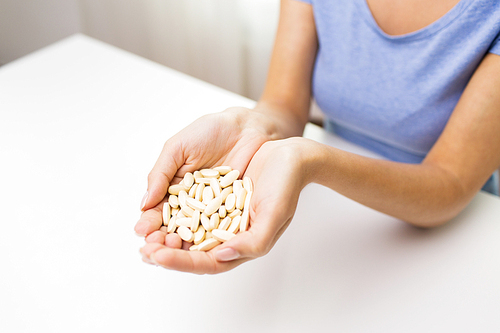 healthy eating, medicine, health care, food supplements and people concept - close up of woman hands with medication or pills at home