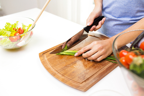 healthy eating, cooking, vegetarian food, dieting and people concept - close up of woman chopping green onion with knife on wooden cutting board