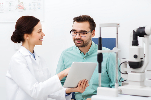 health care, medicine, people, eyesight and technology concept - female optician with tablet pc computer and man in glasses at eye clinic or optics store