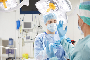 surgery, medicine and people concept - nurse assisting surgeon and helping with gloves in operating room at hospital