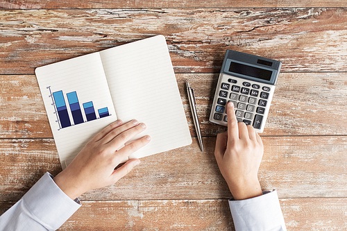 business, education, people and technology concept - close up of female hands with calculator, pen and chart drawing in notebook on table