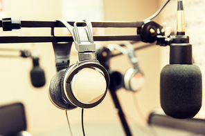 technology, electronics and audio equipment concept - close up of headphones and microphone at recording studio or radio station