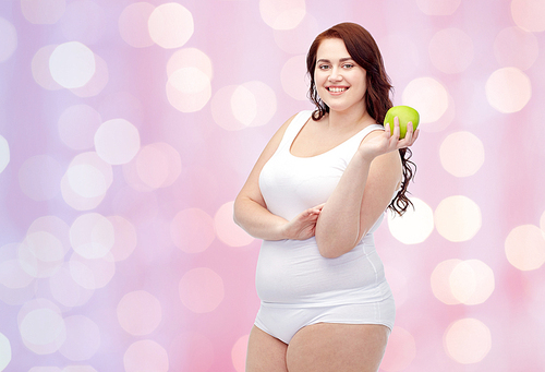 weight loss, diet, slimming, healthy eating and people concept - happy young plus size woman in underwear with green apple over pink holidays lights background