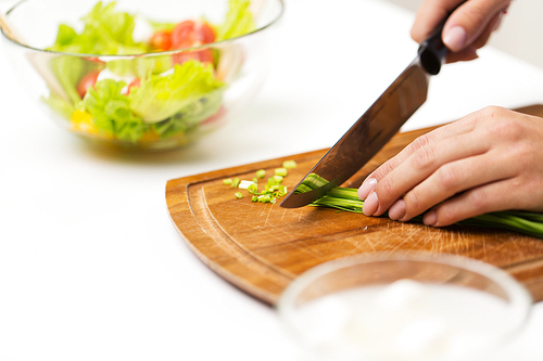 healthy eating, cooking, vegetarian food, dieting and people concept - close up of woman chopping green onion with knife on wooden cutting board