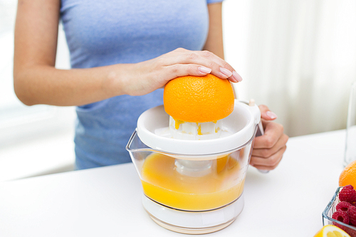 healthy eating, vegetarian food, dieting and people concept - close up of woman with squeezer squeezing orange juice at home