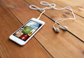 technology, music, gadget and object concept - close up of white smartphone and earphones on wooden surface with web applications on screen