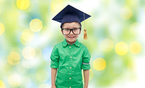 childhood, school, education, learning and people concept - happy boy in bachelor hat or mortarboard over green lights background