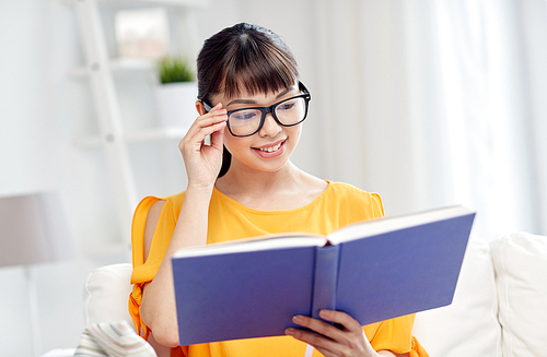 education, knowledge, vision, literature and people concept - smiling young asian woman or student girl in glasses reading book at home