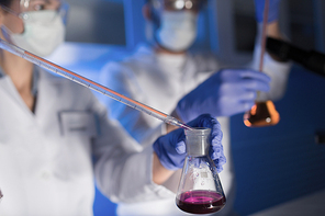 science, chemistry, biology, medicine and people concept - close up of young scientists with pipette and flasks making test or research in clinical laboratory
