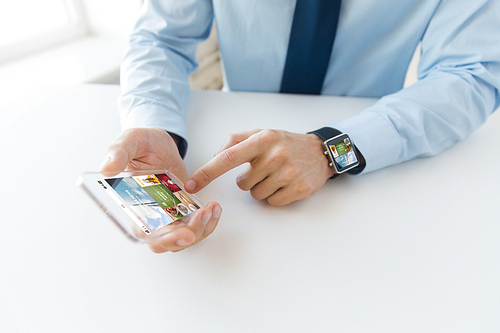 business, technology, media and people concept - close up of male hand holding and showing transparent smart phone and watch at office with web applications on screen