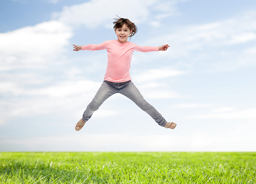 happiness, childhood, freedom, movement and people concept - happy little girl jumping in air over blue sky and grass background