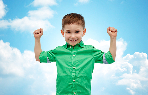 childhood, power, gesture and people concept - happy smiling little boy with raised hands showing his power  over blue sky and clouds background