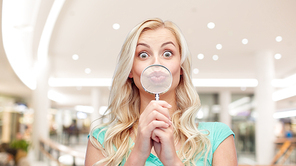 fun, emotions, expressions and people concept - happy smiling young woman or teenage girl having fun with magnifying glass over mall or shopping center background