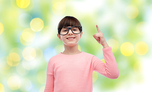childhood, school, education, vision and people concept - happy little girl in eyeglasses pointing finger up over green lights background