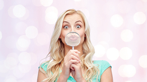 fun, emotions, expressions and people concept - happy smiling young woman or teenage girl having fun with magnifying glass over pink holidays lights background