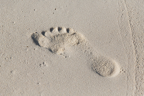 travel, adventure, summer vacation and beach concept - human footprint on beach sand