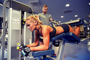 sport, fitness, bodybuilding, teamwork and people concept - young woman and personal trainer flexing muscles on leg curl machine in gym