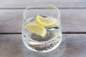 drink and refreshment concept - glass of sparkling water with lemon slices on table