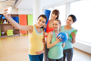 pregnancy, sport, fitness, people and healthy lifestyle concept - group of happy pregnant women with sports stuff taking selfie by smartphone in gym