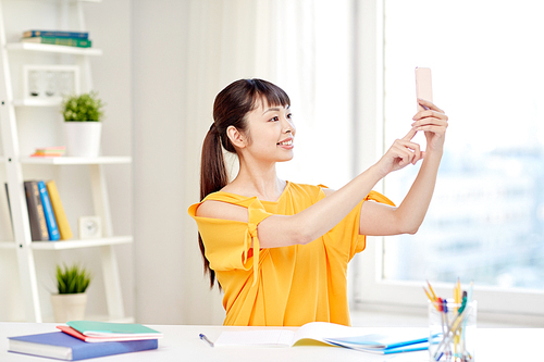 people, education, high school and learning concept - happy asian young woman student taking selfie with smartphone at home