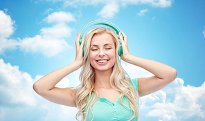 technology and people concept - happy young woman or teenage girl with headphones listening to music over blue sky and clouds background