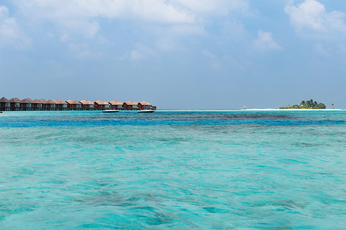 travel, tourism, vacation and summer holidays concept - bungalow huts in sea water on exotic resort beach