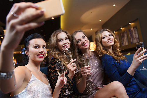 celebration, friends, bachelorette party, technology and holidays concept - happy women with champagne glasses and smartphone taking selfie at night club