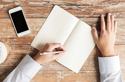 business, education, people and technology concept - close up of female hands with notebook and smartphone on table