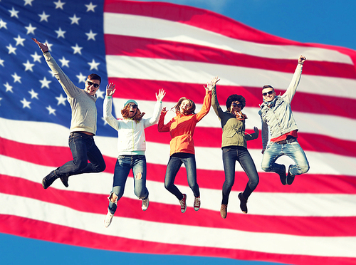 people, freedom, happiness and teenage concept - group of happy international friends in sunglasses jumping high over american flag background