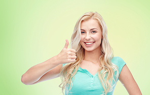 positive gesture and people concept - smiling young woman or teenage girl showing thumbs up over green natural background