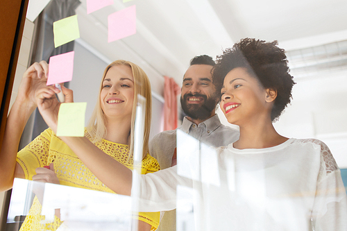 business, startup, planning, management and people concept - happy international creative team writing on stickers at office glass board