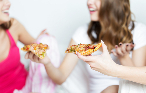 friendship, people, pajama party and junk food concept - close up of happy friends or teenage girls eating pizza at home