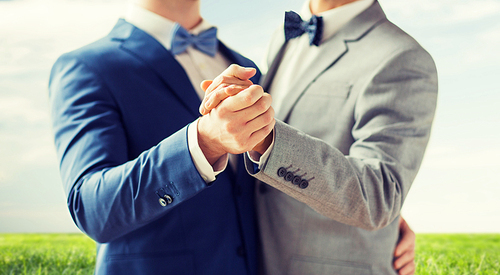 people, homosexuality, same-sex marriage and love concept - close up of happy male gay couple holding hands and dancing over blue sky and grass background