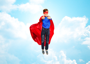 happiness, freedom, childhood, movement and people concept - boy in red super hero cape and mask flying in air and showing thumbs up over blue sky and clouds background