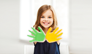 education, school, art and happiness concept - little student girl showing hands in yellow and green color at school