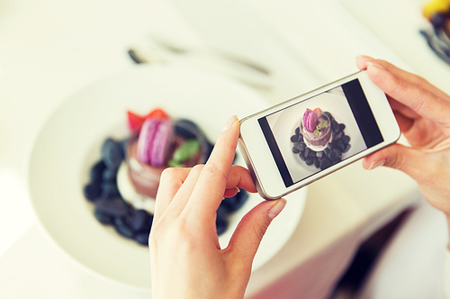 people, holidays, technology, food and lifestyle concept - close up of woman with smartphone taking picture of dessert at restaurant