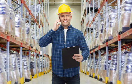 wholesale, logistic, business, export and people concept - smiling businessman with clipboard calling on smartphone over warehouse background
