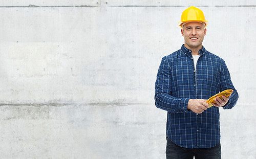 repair, building, construction, people and maintenance concept - smiling man in helmet with gloves over gray concrete wall background