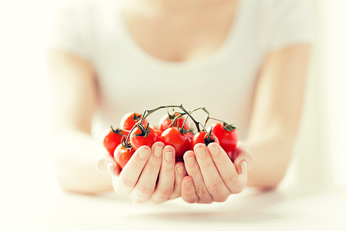 healthy eating, dieting, vegetarian food and people concept - close up of woman hands holding cherry tomatoes bunch at home