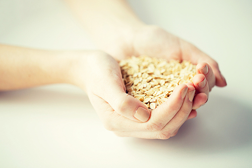 healthy eating, dieting, vegetarian food and people concept - close up of woman hands holding oatmeal flakes at home