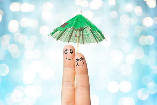 gesture, love, holidays, summer vacation and body parts concept - close up of two fingers with cocktail umbrella decoration over blue holidays lights background