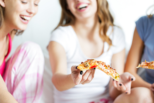 friendship, people, pajama party and junk food concept - close up of happy friends or teenage girls eating pizza at home