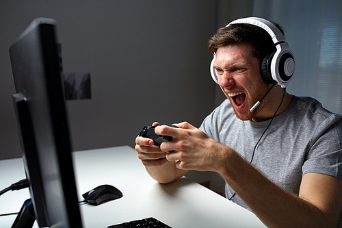 technology, gaming, entertainment, play and people concept - angry screaming young man in headset with controller gamepad playing computer game at home and streaming playthrough or walkthrough video