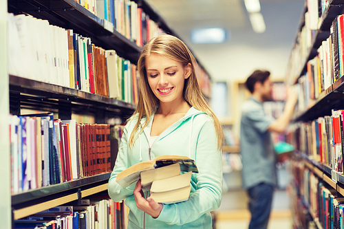 people, knowledge, education and school concept - happy student girl or young woman with book in library